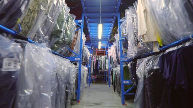 Warehouse with clothes. The clothes are hung in rows in the warehouse. Clothes in the warehouse of the factory. industrial interior