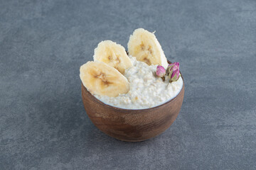 A wooden bowl of oatmeal porridge with slices of banana