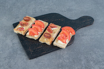 A black wooden board of crispy toasts with tomatoes