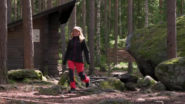 Woman walking towards the camera in front of campfire site and lean-to shelter of Sorsakolu in Evo Hiking Area, H&auml;meenlinna, Finland.