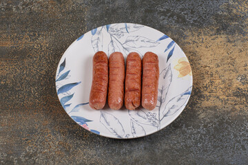Grilled tasty sausages on colorful plate