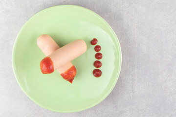 Two boiled sausages with ketchup on green plate