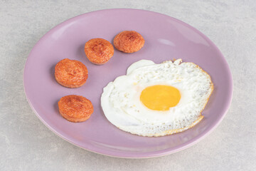 Sliced grilled sausages and fried egg on purple plate