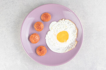 Sliced grilled sausages and fried egg on purple plate