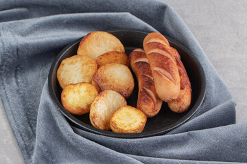 Fried sausages and potatoes on black plate
