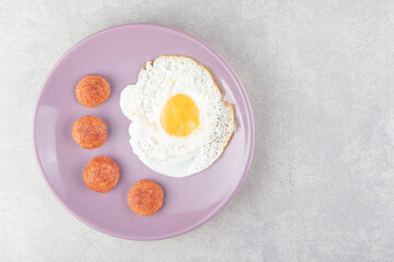 Sliced grilled sausages and fried egg on purple plate