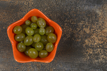 Tasty green grapes in orange bowl