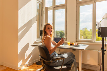 Happy blonde freelancer using cellphone near orange juice and breakfast at home.