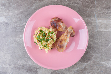 Two pieces of drumstick next to pasta on a plate , on the marble background