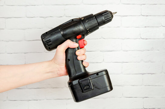 Tool, Electric Screwdriver In Female Hand On Background Of White Brick Wall. Drill With Battery Pack