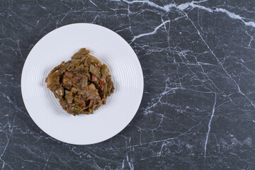 Marinated vegetables on white plate over black background