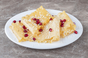 Pomegranate arils with lasagna sheets on the plate, on the marble background