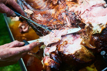 Chef Hands cutting whole grilled pork for steaks with knife. Pig grilled traditional coal and fire....