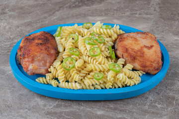 Two pieces of meat and peppered fusilli pasta on the wooden tray , on the marble background