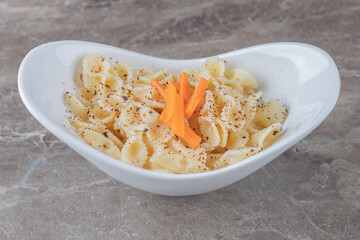 Toothsome farfalle pasta with spicy tomato sauce in bowl, on the marble background