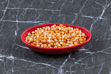 Pile of fresh corn seeds in red bowl over black stone background