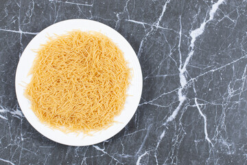 Uncooked raw vermicelli on white plate over black background