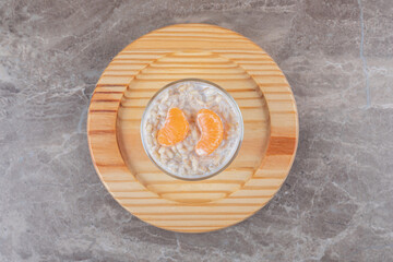 Porridge with two orange slices in a glass on a wooden plate, on the marble background