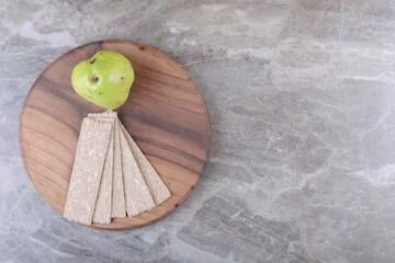 Crispbreads and pear on the board, on the marble background