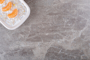 Orange slices on top of porridge in a bowl, on the marble background
