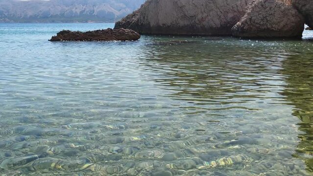 View of rocks sticking out of the water on Beritnica beach on the Croatian island of Pag, slow motion