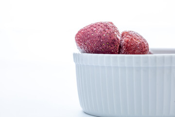 frozen strawberry in white ceramic bowl on white background with copy space 
