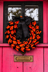Orange and black wreath Halloween decoration on vintage pink painted rustic exterior door - 534010292