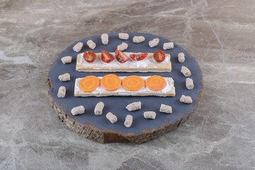 Sliced carrots, and tomatoes on crispbreads, surrounded by crumb on the board, on the marble...