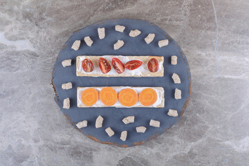 Sliced carrots, and tomatoes on crispbreads, surrounded by crumb on the board, on the marble background