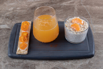 Porridge with two orange slices in a glass on a wooden tray next to orange juice, on the marble background