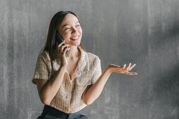Fototapeta premium Beautiful Asian woman working at a coffee shop with her laptop and talking on her smartphone and smiling. A woman works on a computer and uses a mobile phone while sitting at a coffee shop.