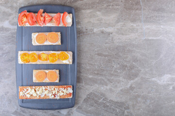 Sliced carrots, cheese and tomatoes on crispy breads on the wooden tray, on the marble background