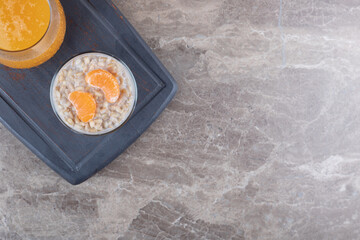 Porridge with two orange slices in a glass on a wooden tray next to orange juice, on the marble background