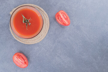 Top view. Glass of fresh tomato juice and tomato slices on a grey background