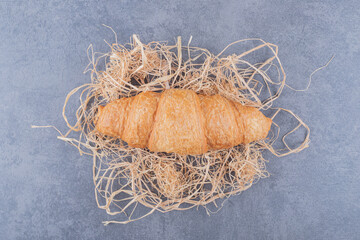 Top view of fresh French croissant on decorative straw over grey background