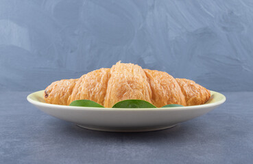 Fresh French croissant on white plate over grey background
