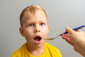 little boy takes medicine from a spoon