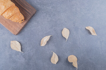 Close up photo of French croissant on grey wooden and decorative leave over grey background