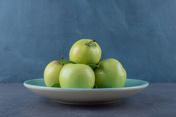 Close up photo of green apple on plate over grey background
