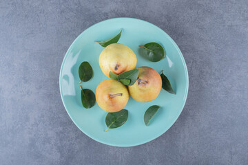 Top view of fresh organic pears wit leaves on blue plate over grey background