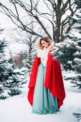 A beautiful girl in red fairy-tale clothes walks through a snow-covered forest