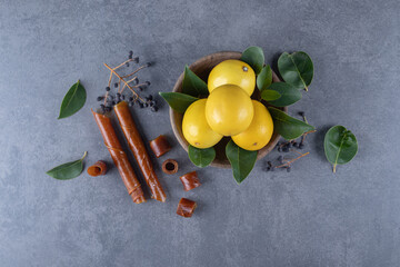Bowl of fresh lemons and green leaves over grey background