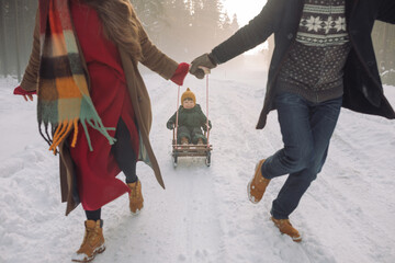 Parents ridding their little son on a sled in a snowy forest. Holiday atmosphere. Winter family activities.