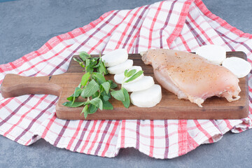 Uncooked chicken fillet with radish slices on wooden board