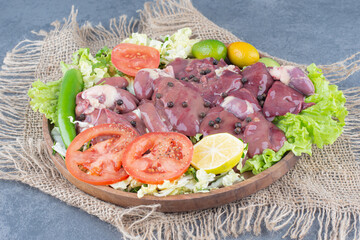 Raw meat pieces and vegetables on wooden plate