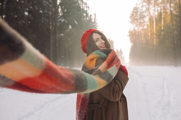 Portrait of beautiful happy woman walking in the forest on winter day. Young girl in a red beret, warm coat with a bright scarf. Winter holidays mood.