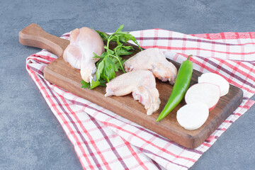 Raw chicken wings and leg on wooden board