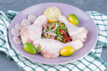 Raw chicken legs with vegetables on purple plate