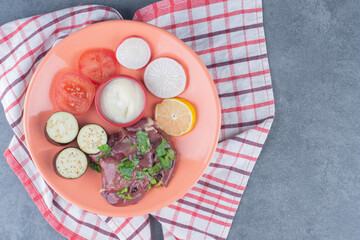 Raw meat and sliced fresh vegetables on orange plate