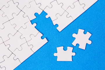 Missing jigsaw puzzle pieces. Business concept. Fragment of a folded white jigsaw puzzle and a pile of uncombed puzzle elements against